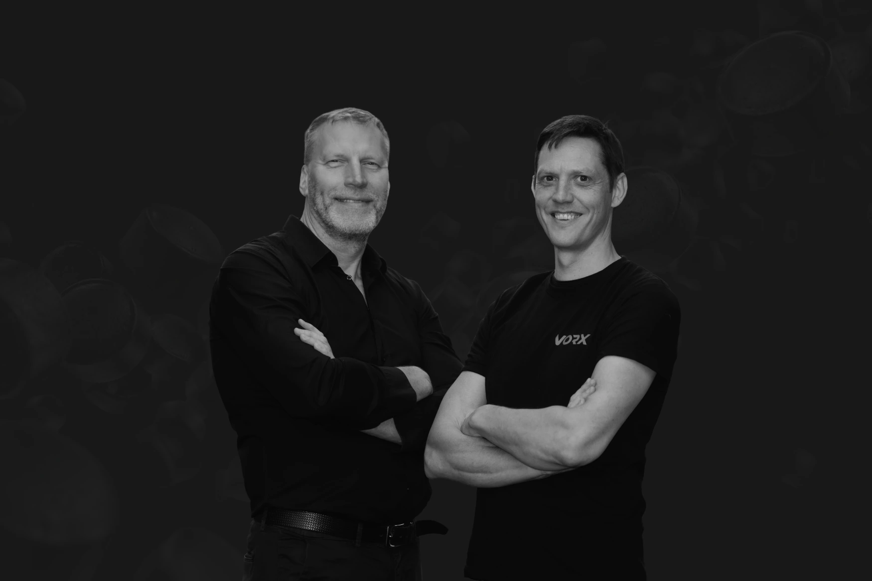 Rihards Jordans (left) and Janis Abols (right) of VORX, arms crossed, in black shirts against a dark background.